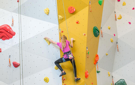 Jente med rosa trøye klatrer topptau på gul vegg